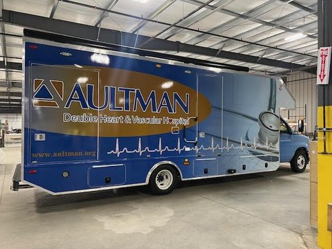 Mobile medical clinic on a Ford E-Series cutaway, blue Aultman wrap, driver side, in the HLE plant