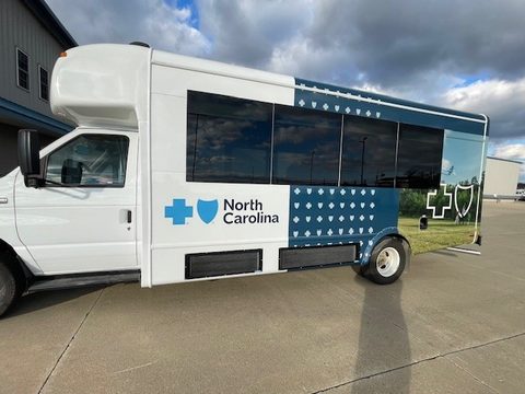 Mobile outreach bus on a Ford E-Series cutaway, navy Blue Cross NC wrap, driver side, outside