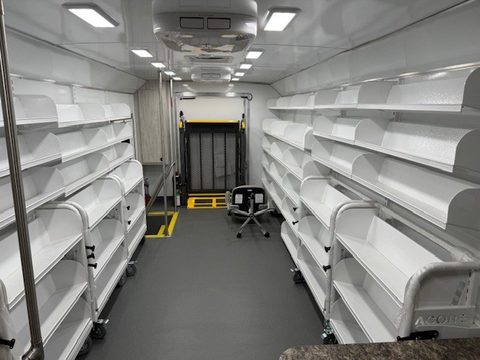 Bookmobile interior: white library shelving both sides, looking aft to the lift