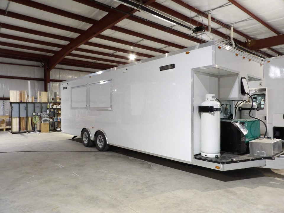 White bumper-pull food trailer with generator and propane on the tongue, in the plant