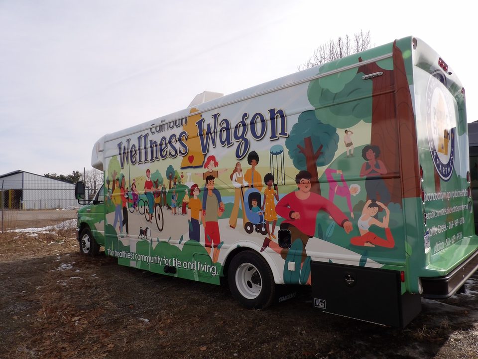 Wellness Wagon on a Ford E-450 cutaway, green illustrated wrap, front three-quarter, outside