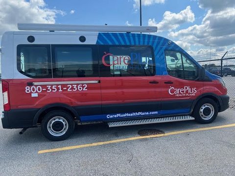 CarePlus Health Plans outreach van on a Ford Transit, red white and blue wrap, driver side, outside under blue sky