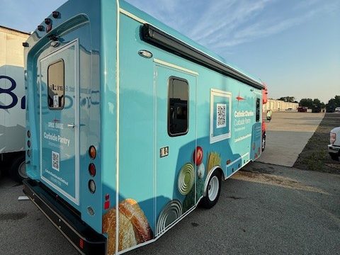 Mobile food pantry, rear three-quarter, teal wrap, awning on the curb side