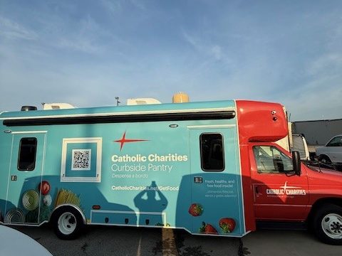Curbside Pantry food pantry on a Ford E-Series cutaway, red cab and teal wrap, driver side, outside at sunset