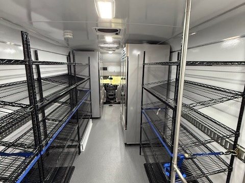Food pantry interior: wire shelving both sides of the aisle, cooler at the front
