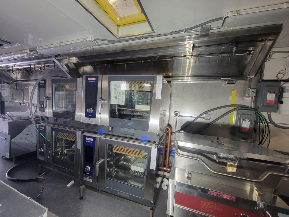 Stacked combination ovens under a stainless range hood inside the kitchen container