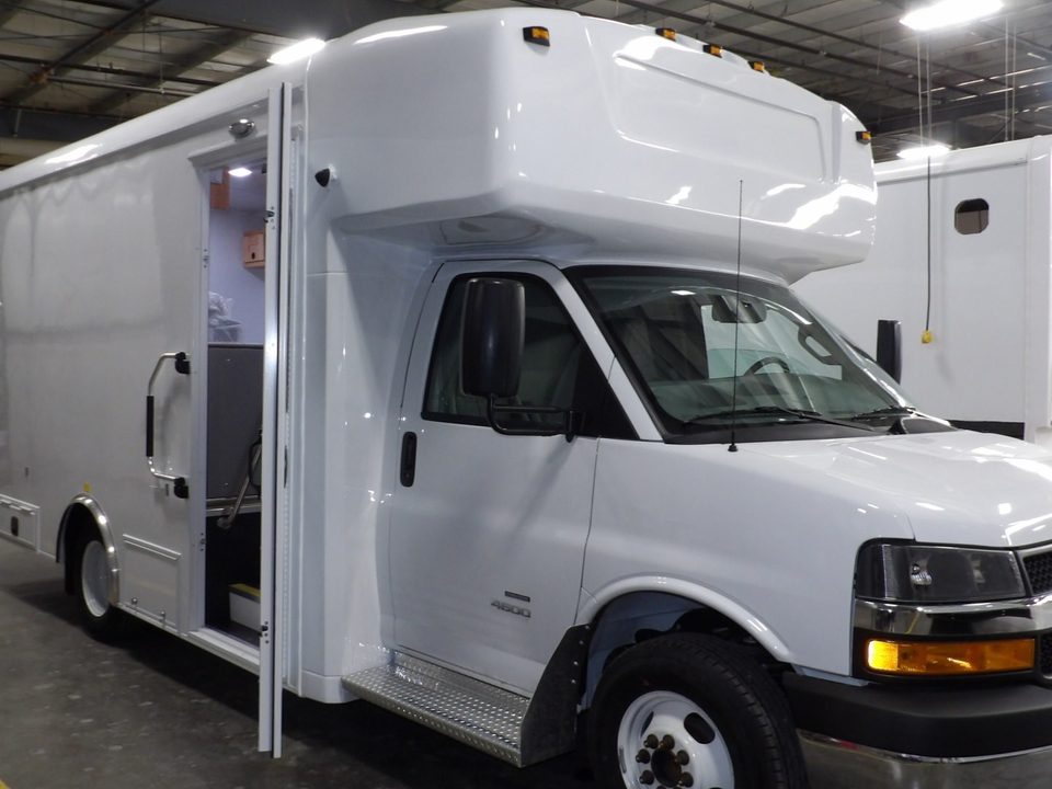 White mobile classroom on a Chevrolet Express cutaway, front three-quarter, entry door open, in the HLE plant