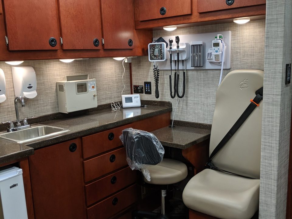 Exam room with cherry cabinetry, sink and exam chair inside a mobile clinic