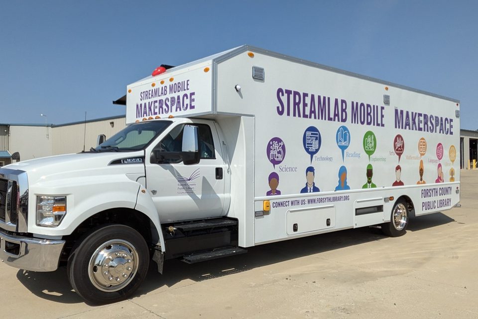 STREAMlab Mobile Makerspace on a Ford F-650, wrapped white and purple, front three-quarter, blue sky