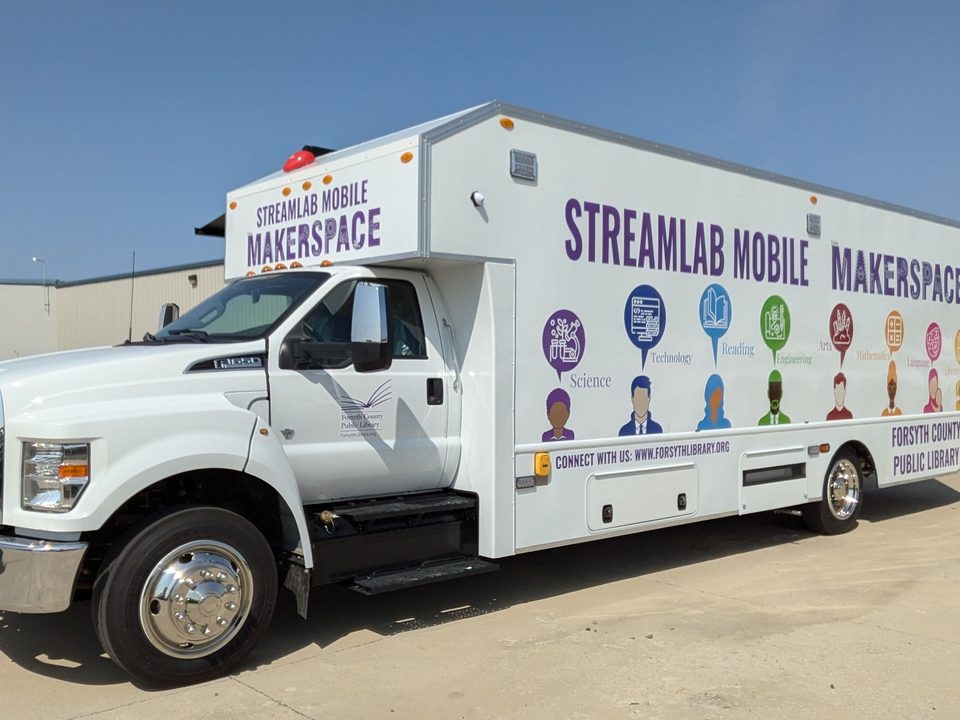STREAMlab Mobile Makerspace on a Ford F-650, wrapped white and purple, front three-quarter, blue sky