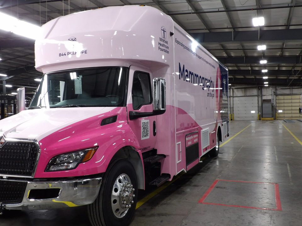 Mobile mammography unit on an International MV, wrapped pink and white, front three-quarter, in the HLE plant