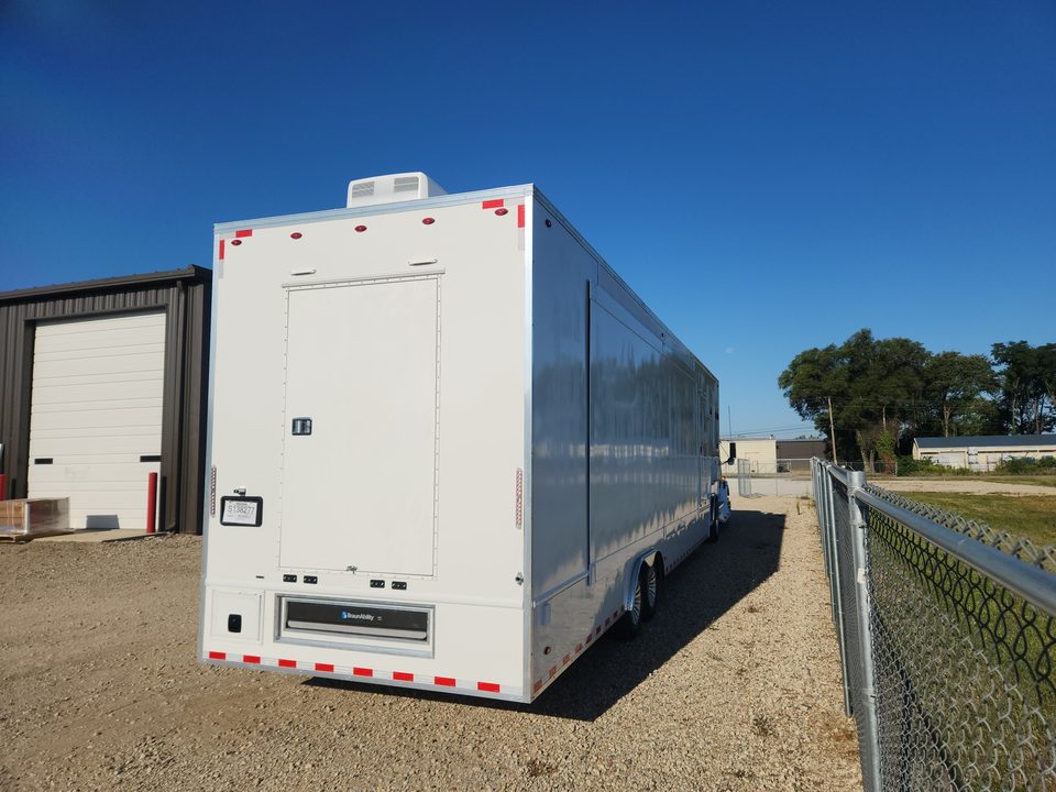 White enclosed bumper-pull trailer outside the HLE plant, rear three-quarter, blue sky