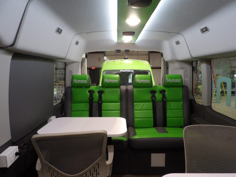 Van interior: dinette table, green and gray bench seat, chair