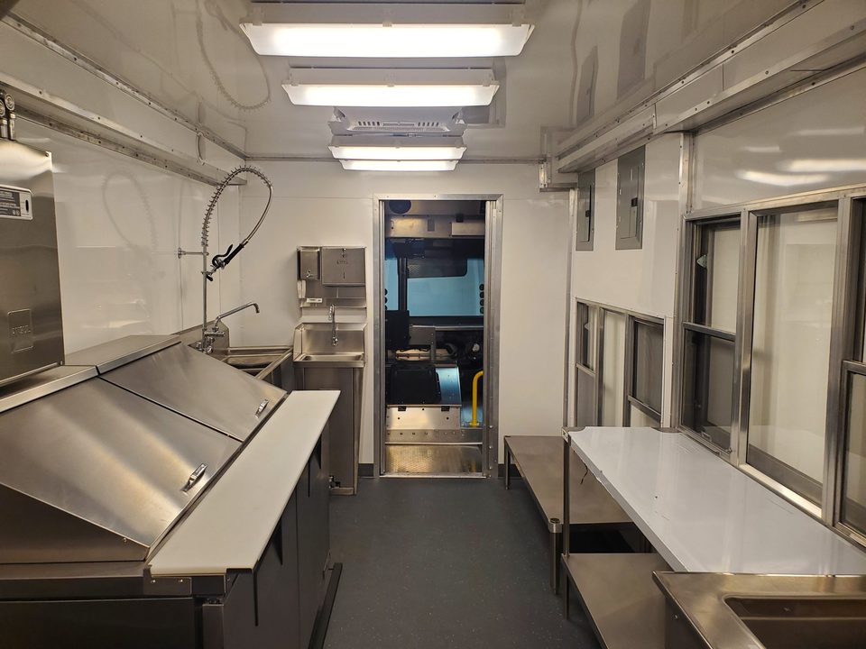 Mobile kitchen interior: stainless counters, hood, hand sink, pass-through window