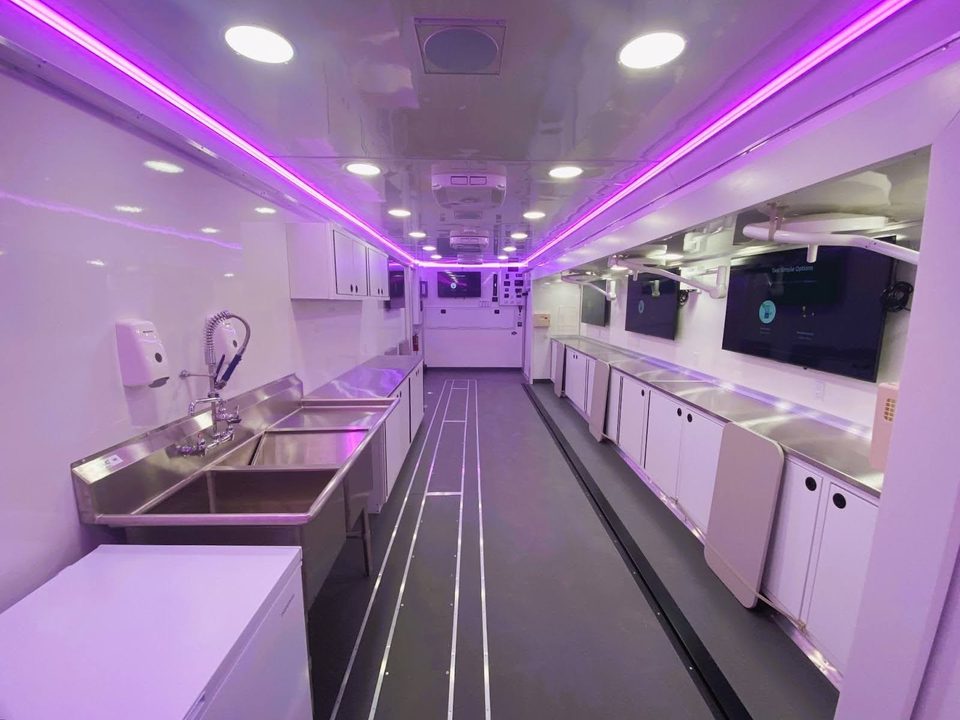 Interior of a mobile lab: stainless counters, sink, overhead cabinets, LED cove lighting