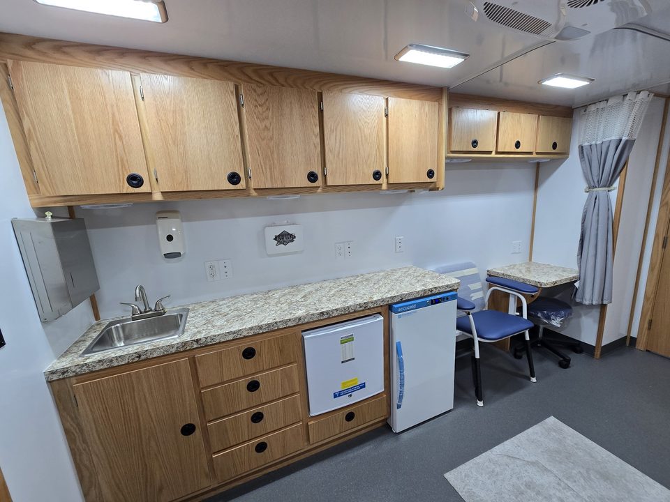 Clinic interior: counter with sink, two refrigerators, oak cabinets, exam chair