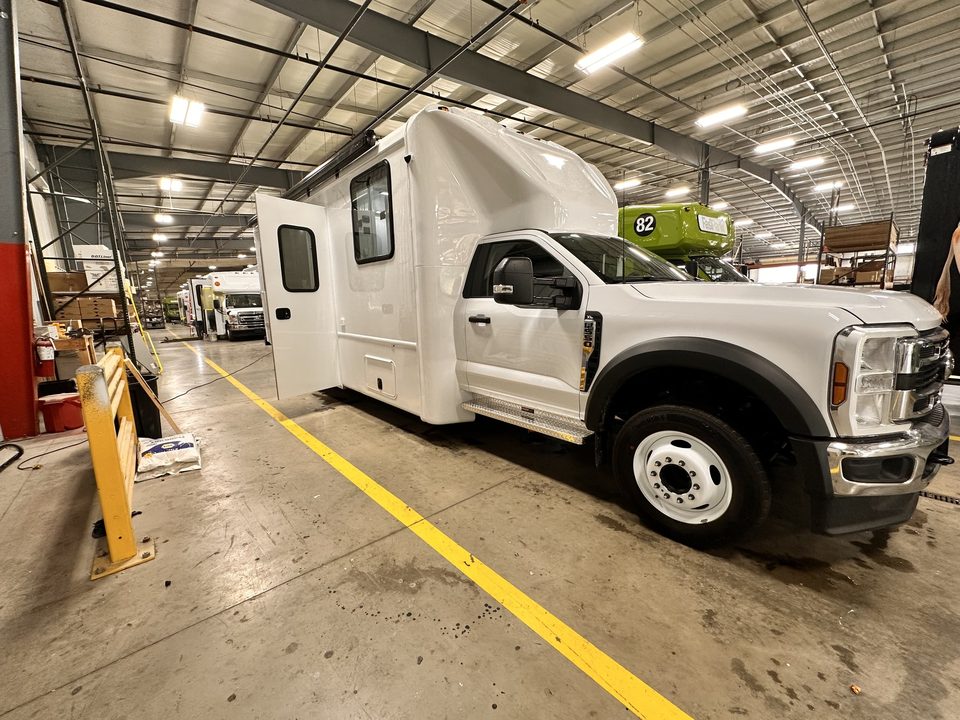 White mobile outreach unit on a Ford F-550, front three-quarter, curbside entry door, in the HLE plant