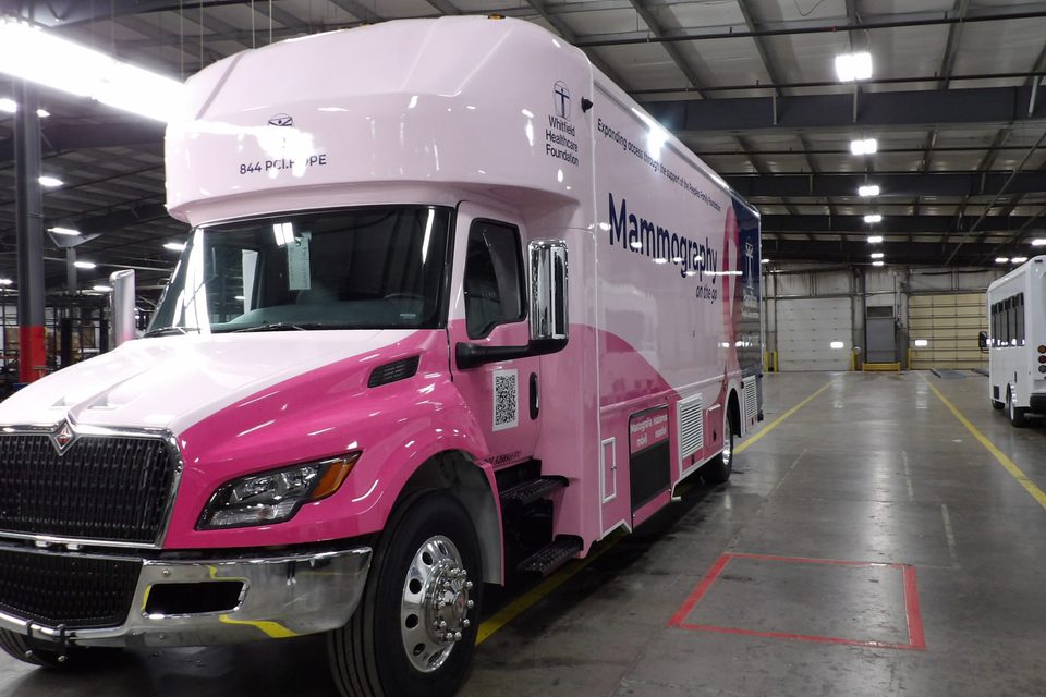 Mobile mammography unit on an International MV, wrapped pink and white, front three-quarter, in the HLE plant