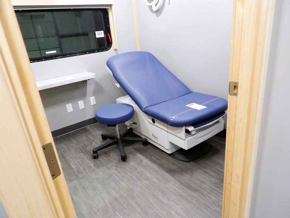 Exam room with power exam table and stool inside the health unit