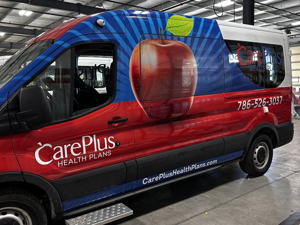 Ford Transit outreach van wrapped red and blue with an apple graphic, driver side, in the plant