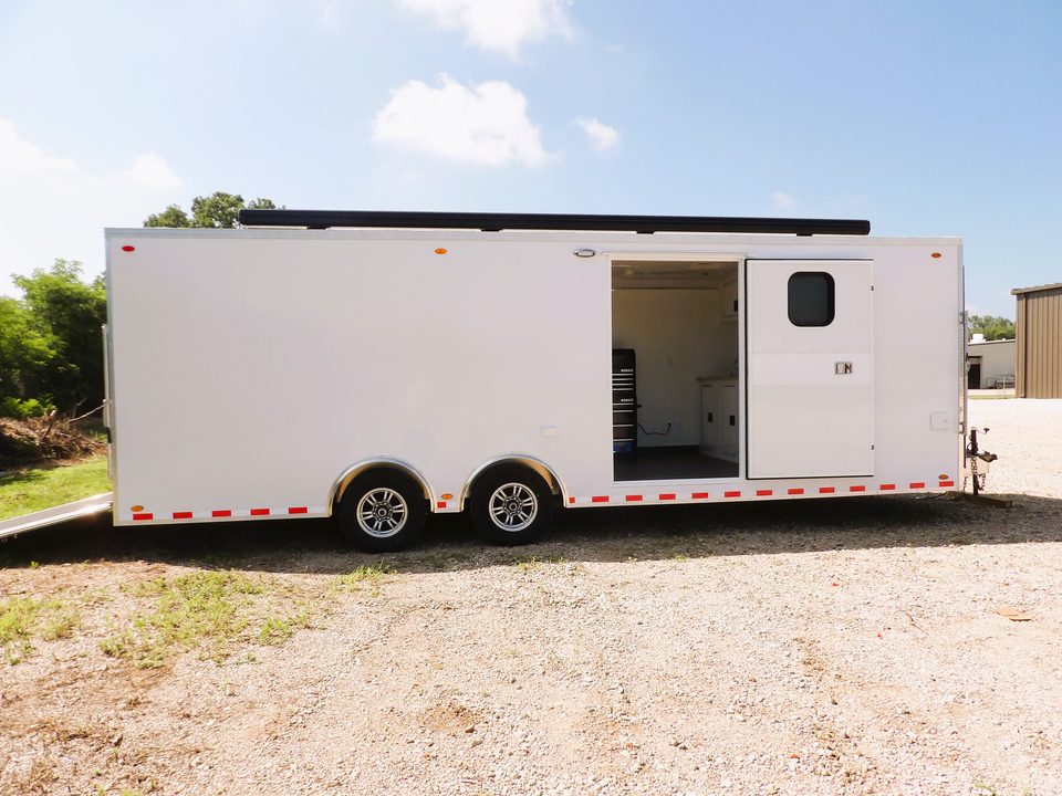 White bumper-pull trailer outside with the side door open, awning rolled on the roof