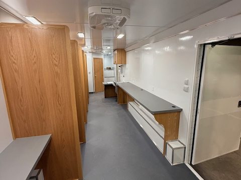 Voting trailer interior: wood voting booths along one wall, counter opposite