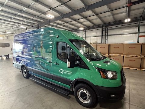 Mobile dental van on a Ford Transit, green and blue Tooth Transit wrap, front three-quarter, in the HLE plant