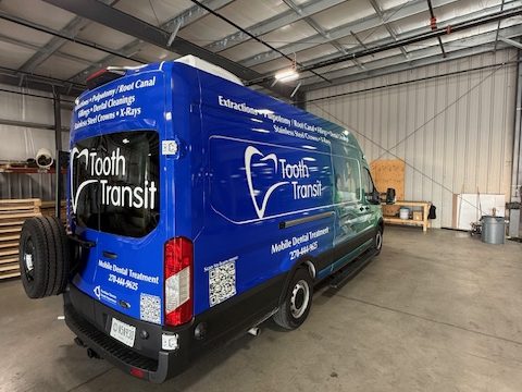 Mobile dental van, rear three-quarter, blue wrap listing services