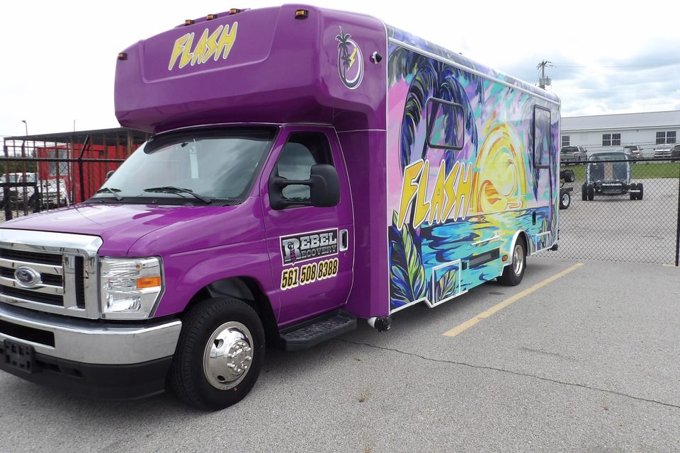 Mobile health unit on a Ford E-Series cutaway, purple FLASH wrap with palm trees, front three-quarter