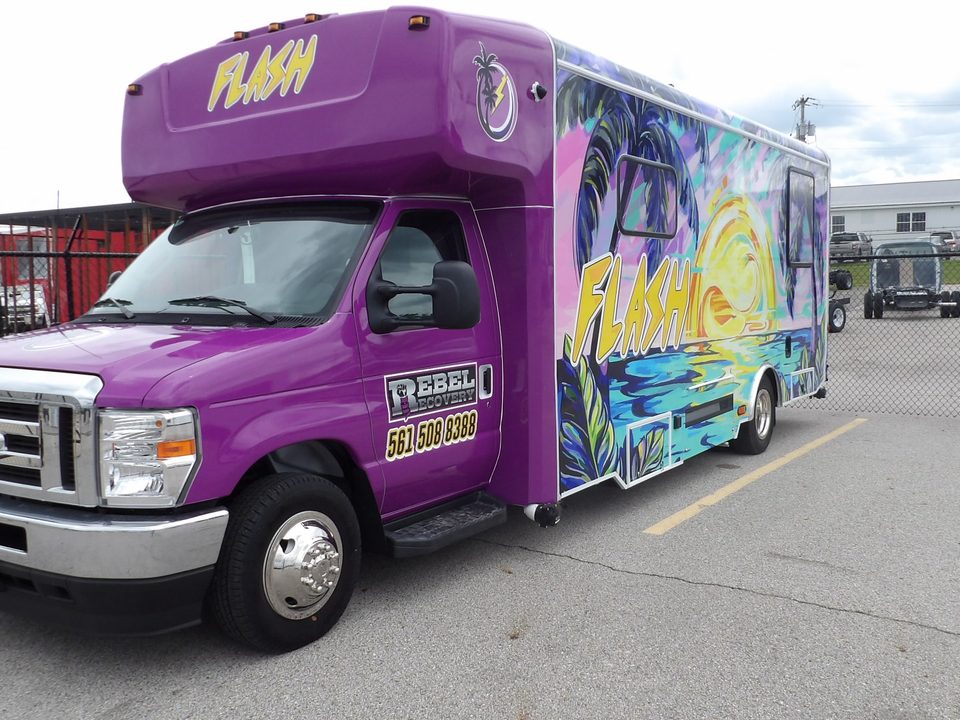 Mobile health unit on a Ford E-Series cutaway, purple FLASH wrap with palm trees, front three-quarter