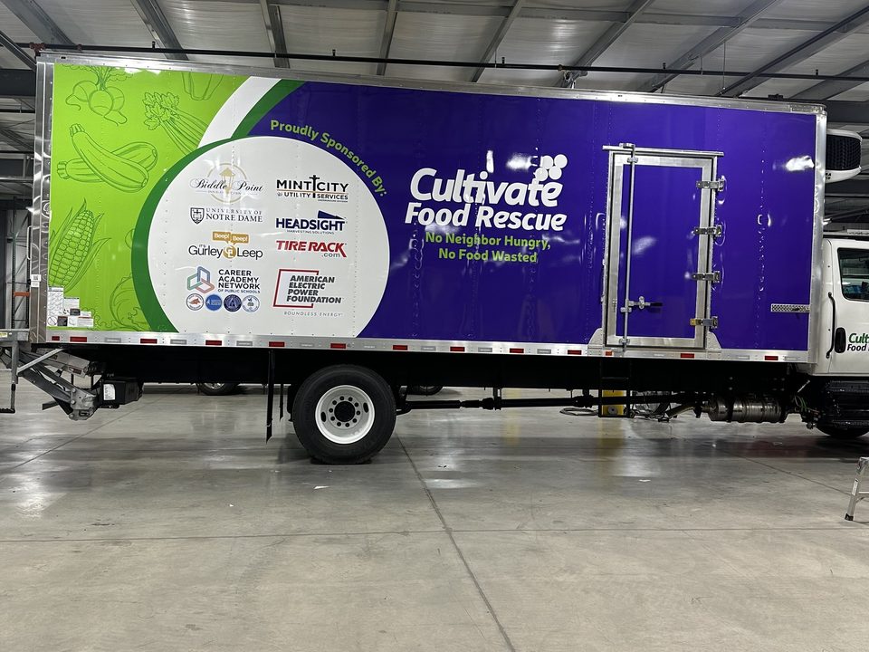 Refrigerated box truck with a purple and green food-rescue wrap, in the wrap shop