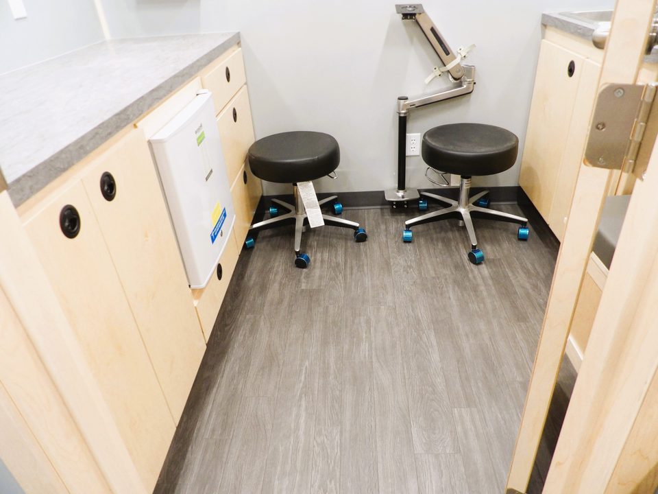 Exam room with stools, refrigerator and wall-mounted diagnostic arm